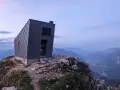 Il bivacco Giacomelli alla Madonnina, una struttura moderna su una cresta rocciosa, domina un paesaggio montano al tramonto.