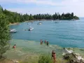 La baia delle Sirene a Garda, con gente che nuota e barche sull'acqua cristallina, sotto un cielo azzurro.