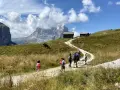 Famiglia in escursione su sentiero facile a Selva di Val Gardena, con baite e montagne sullo sfondo.