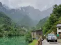 Il lago della Stua, incastonato tra montagne nebbiose e foreste lussureggianti, con una casa e un'auto parcheggiata vicino.