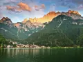 Un incantevole giro del lago di Alleghe, con il paese incastonato tra boschi e montagne maestose illuminate dal sole al tramonto.