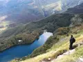 Un escursionista ammira il lago Santo Modenese, circondato da boschi autunnali e montagne.