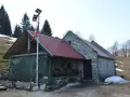 Bivacco Vallon Scuro: rifugio in pietra con tetto rosso, pannelli solari e telo verde. Un uomo si ripara dal freddo.