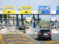 Casello autostradale con corsie Telepass e carte. Un'auto nera si avvicina, sperando che il suo Telepass non funzioni per evitare una multa.