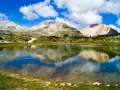 Un limpido lago di limo riflette montagne maestose e un cielo azzurro con nuvole bianche.