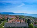 Vista aerea di Moniga del Garda, con il castello medievale in primo piano, il lago e le montagne sullo sfondo.