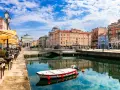 Un'incantevole vista di Trieste: un canale con una barca, caffè all'aperto e palazzi storici. Ecco cosa vedere a Trieste per un'esperienza indimenticabile.