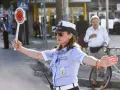 Agente di polizia locale in posizione vigile, braccio alzato per dirigere il traffico.