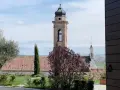 Torre campanaria e un albero in fiore, scorcio di un borgo tra le colline. Castagnole delle Lanze cosa vedere: un paesaggio incantevole.