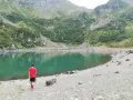 Ragazzo in maglietta rossa ammira il **lago di Erdemolo**, circondato da verdi pendii montuosi e rocce.