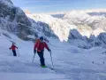 Sciatori scendono da un ripido pendio innevato sul Monte Cristallo, con vette maestose sullo sfondo. La **funivia** è lontana, ma l'avventura è appena iniziata.
