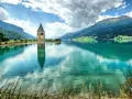 Torre sommersa nel lago di Resia, con montagne verdi e cielo nuvoloso.