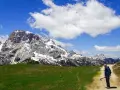 Un uomo con bastoncini da trekking su un sentiero in Trentino, con imponenti montagne innevate sullo sfondo. Un'esperienza di trekking trentino facile e panoramica.