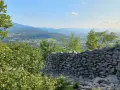 Muro di pietra a secco con vista panoramica su una valle alpina e montagne all'orizzonte.