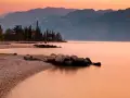 Brenzone sul Garda: cosa vedere? Spiaggia di ciottoli, cipressi e montagne al tramonto sul lago.