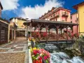 Un pittoresco ponte di legno coperto, adornato di fiori, attraversa un torrente impetuoso. Un incantevole scorcio di cosa vedere in un borgo alpino.