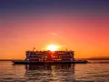 Traghetto in navigazione sul Lago di Garda al tramonto, con il sole che illumina il cielo e il riflesso sull'acqua.