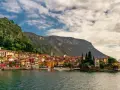 Colorate case affacciate sul lago di Lecco, con montagne verdi sullo sfondo e un cielo nuvoloso.