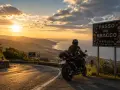 Motociclista al Passo del Bracco al tramonto, con vista sul mare e sulle colline illuminate dalla luce dorata.