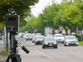 Autovelox mobile come funziona: un dispositivo su treppiede misura la velocità delle auto in transito su una strada alberata.
