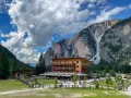 Edificio in legno a Pederu San Vigilio, con montagne imponenti e cielo nuvoloso.