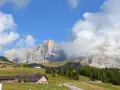 Panorami mozzafiato al Passo Rolle: malghe, boschi e vette imponenti sotto un cielo azzurro con nuvole bianche.