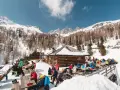 Malga Valcigolera, un rifugio alpino innevato con gente seduta ai tavoli. Per sapere come arrivare, guarda l'immagine.