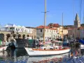 Porto di Muggia cosa vedere: barche a vela, edifici storici e un campanile svettano sotto il cielo azzurro.