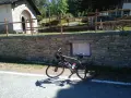 Bicicletta ferma sul ciglio della strada, con un muretto in pietra e un cartello che indica "Colle Braida".