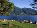 Persone rilassate sui prati e sulle rive di uno dei bellissimi laghi piemontesi, con montagne verdi sullo sfondo.