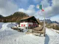 Rifugio Antelao innevato, con tavoli esterni e bandiere. Informazioni su come arrivare al rifugio sono visibili.