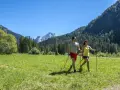 Coppia fa nordic walking in un prato verde con montagne sullo sfondo, ideale per canazei escursioni facili.