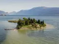 Un'incantevole isola dei conigli sul Lago di Garda, con un piccolo molo e una casetta gialla tra i cipressi.