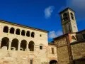 Antica **cella monte** con portici ad archi e torre campanaria sotto un cielo azzurro.