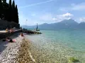 Persone rilassate sulla torri del benaco spiaggia, con acque limpide e montagne sullo sfondo.