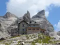 Il rifugio Tuckett e Sella, un'oasi di pietra tra le imponenti vette dolomitiche, accoglie escursionisti sotto un cielo azzurro e nuvoloso.