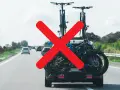 Attenzione al carico sporgente auto! Biciclette sul portabici posteriore, ma una grande X rossa indica un problema di sicurezza.