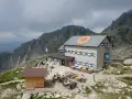 Il rifugio Cima d'Asta, con le sue finestre blu e arancioni, accoglie escursionisti tra rocce e montagne nebbiose.