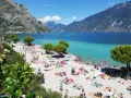 Una vivace spiaggia di Limone sul Garda, con gente che prende il sole e nuota nelle acque turchesi del lago.