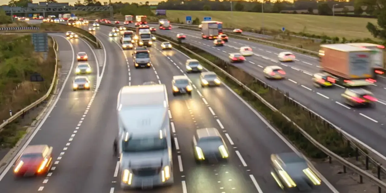 Traffico intenso su un'autostrada al tramonto. Auto e camion sfrecciano, creando scie luminose. Chissà se il limite velocità autostrada 150 dove è rispettato.