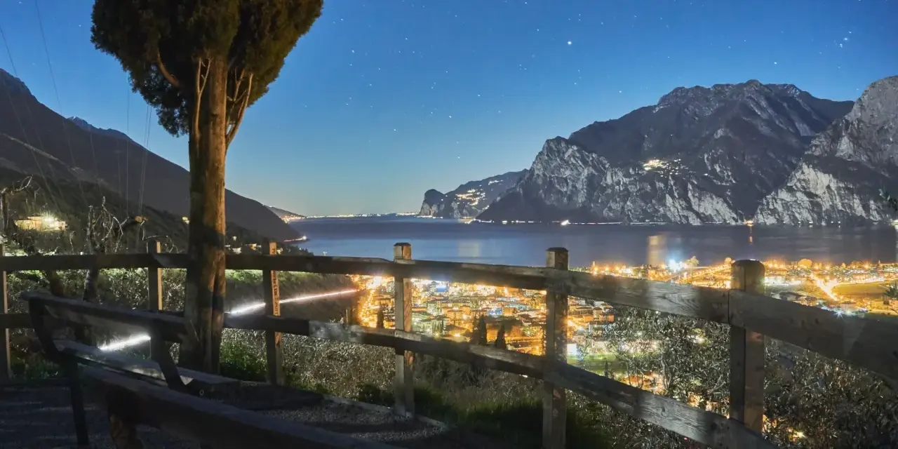 Peschiera del Garda di sera: un panorama mozzafiato con luci scintillanti, montagne imponenti e un cielo stellato. Ideale per una serata romantica.