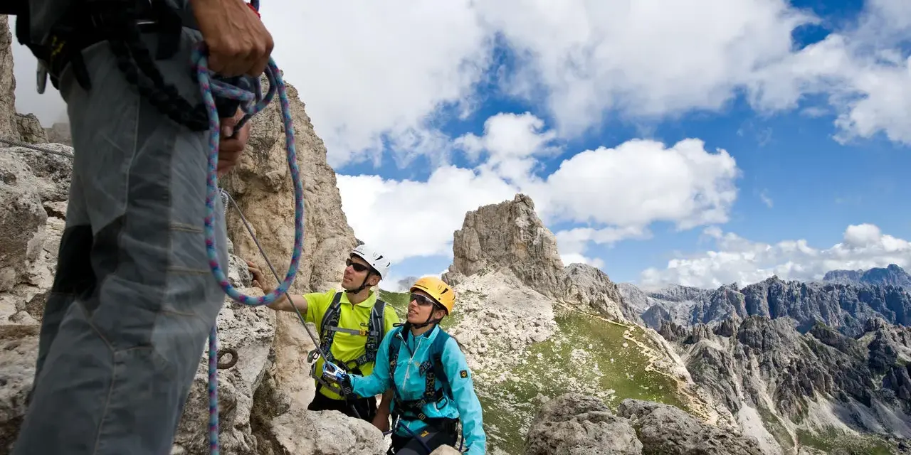 Escursionisti in cordata si godono un giro del Catinaccio, con cime rocciose e cielo azzurro.