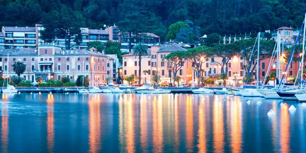 Il lungolago di Toscolano Maderno cosa vedere: hotel storici, palazzi colorati e barche a vela ormeggiate, con riflessi dorati sull'acqua.