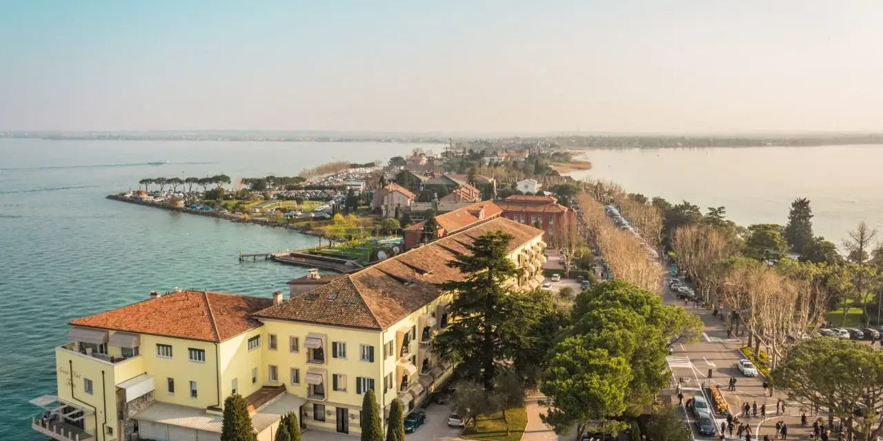 Vista aerea del centro storico di Sirmione, con edifici storici, lago e passeggiata affollata.