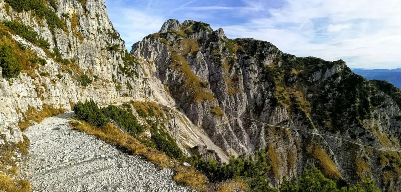 Sentiero roccioso in montagna, parte della strada degli eroi anello, con vegetazione sparsa e cielo azzurro.