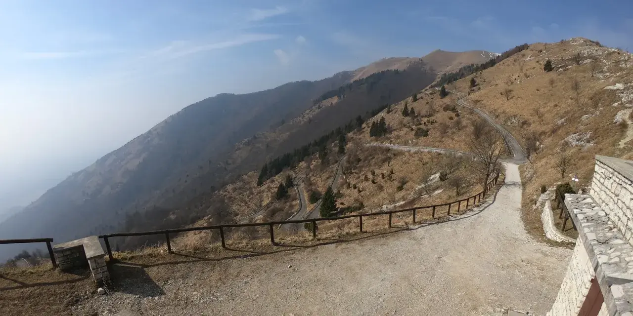 Strada tortuosa sul Monte Palon, Grappa, con vista panoramica sulle montagne e cielo azzurro.