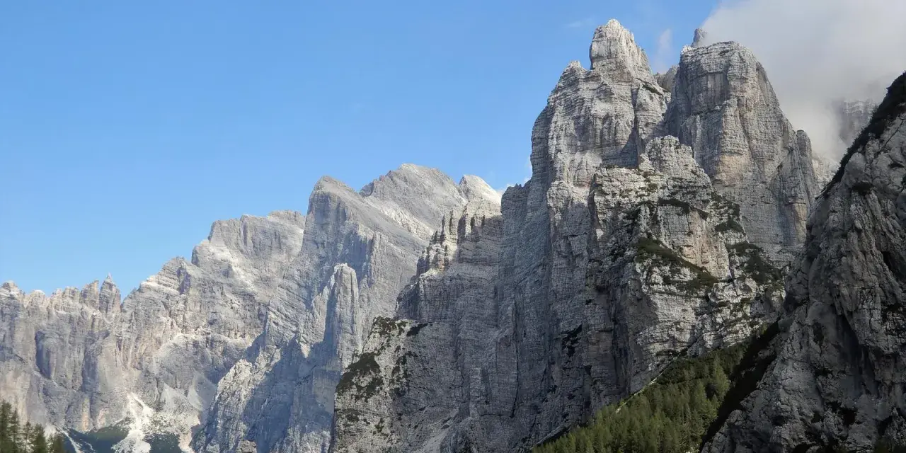 Imponenti cime rocciose dei monti di Framont si stagliano contro un cielo azzurro, con foreste di conifere ai loro piedi.