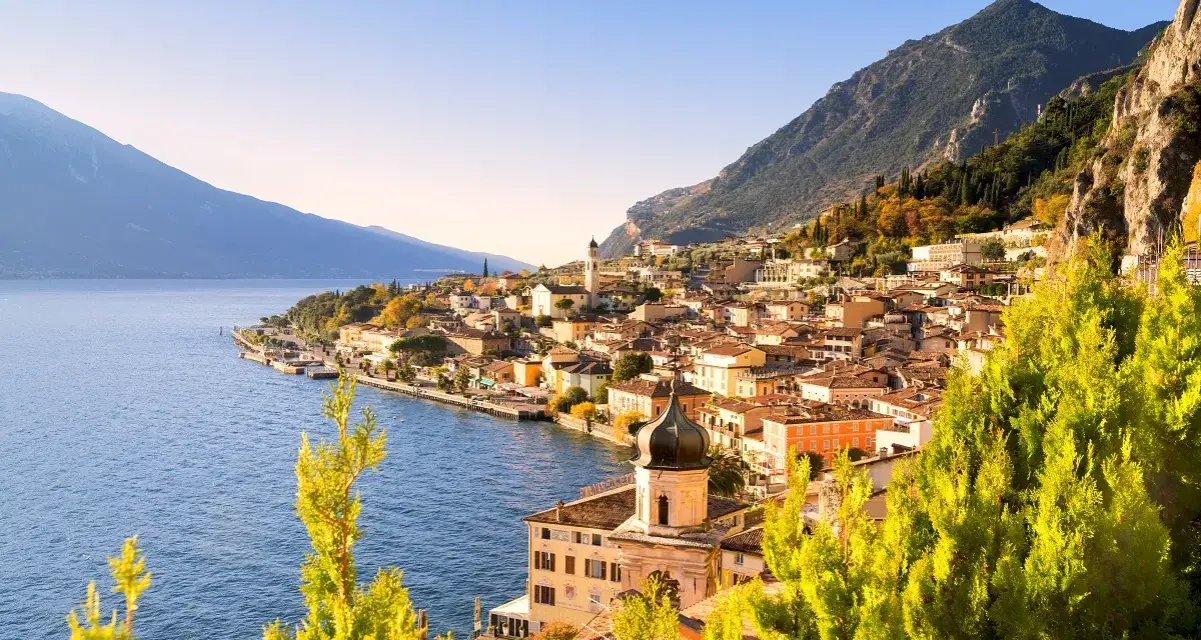 Un perfetto weekend sul lago di Garda: borgo colorato affacciato sull'acqua blu, montagne verdi e cielo limpido.