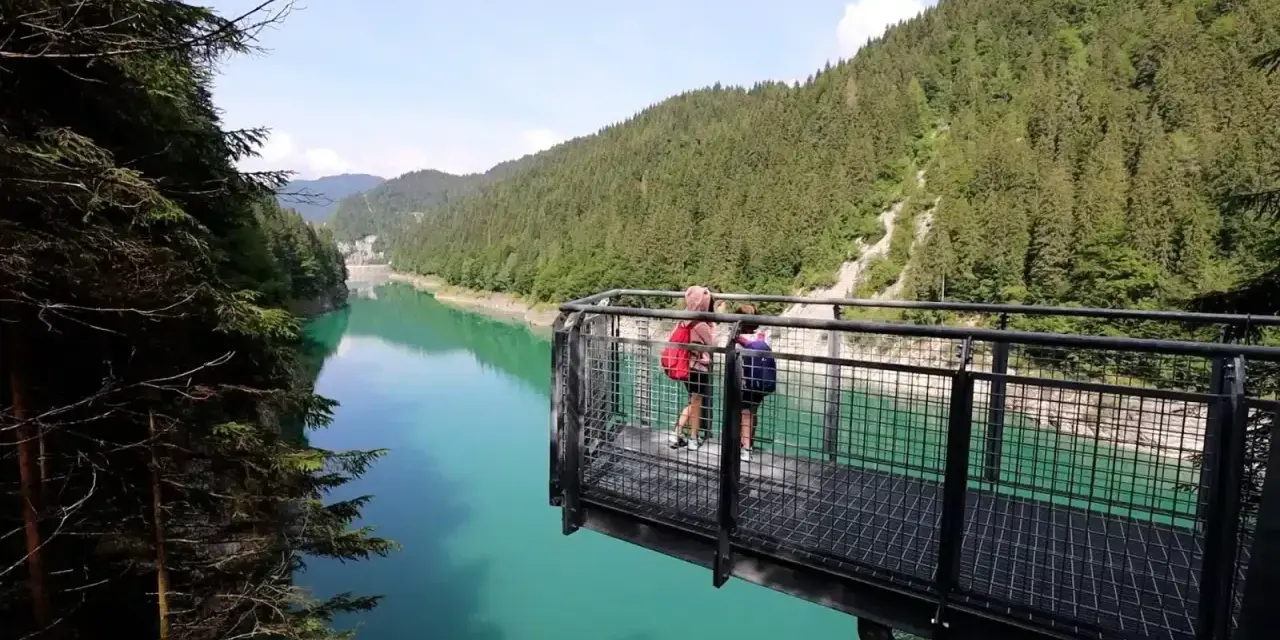 Due persone su una piattaforma panoramica ammirano il lago di Val Noana. Ecco come arrivare a questo splendido lago alpino.