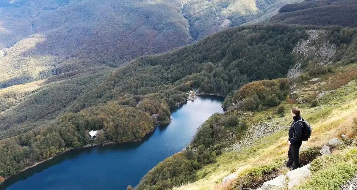 Un escursionista ammira il lago Santo Modenese, circondato da boschi autunnali e montagne.